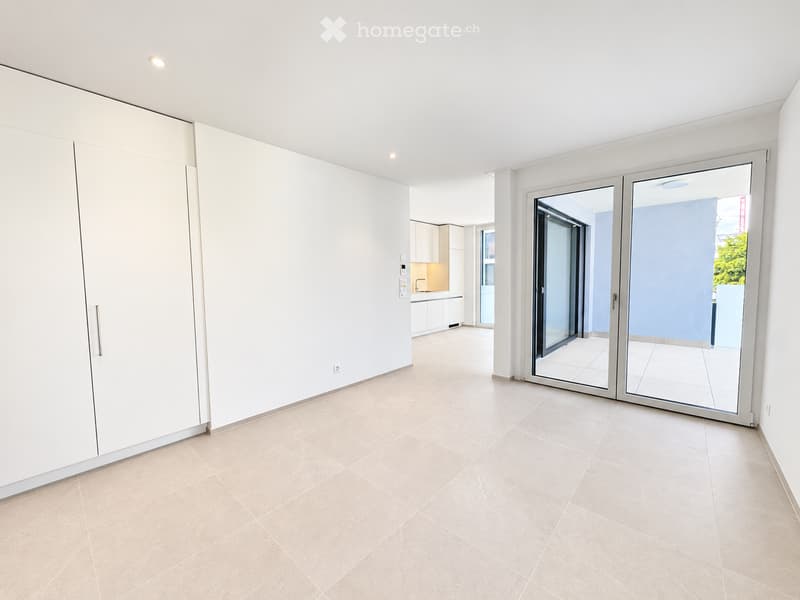 Empty room with white walls, beige tiled floor, large sliding glass doors leading to a balcony, and a built-in wardrobe on one side.