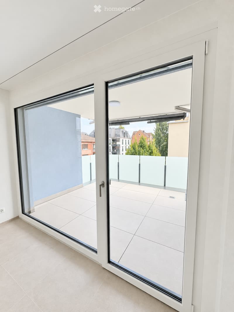 Modern balcony with white tiled flooring, large glass sliding doors, and a sleek, minimalist design.
