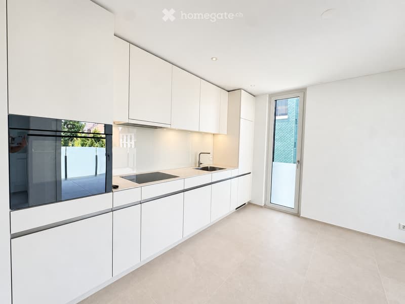 Modern kitchen with white cabinets, a countertop, a sink, and an oven. The space features a large window and a door leading outside.