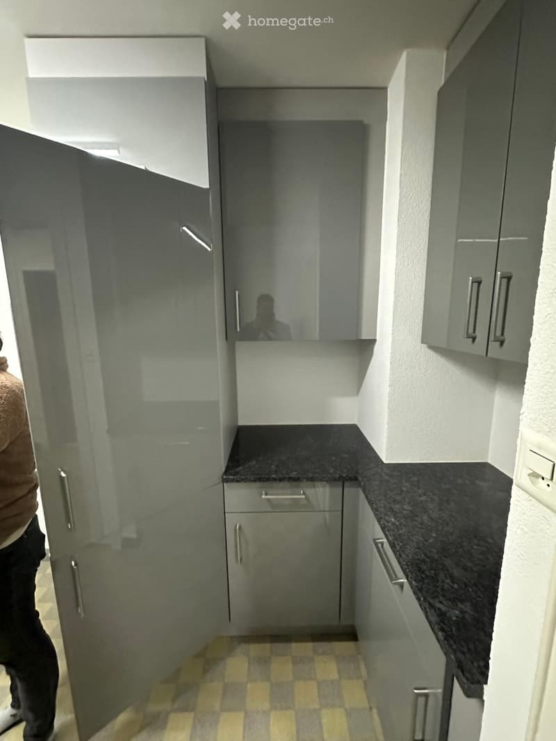 Modern kitchen with grey cabinets, black countertop, and checkered floor tiles.