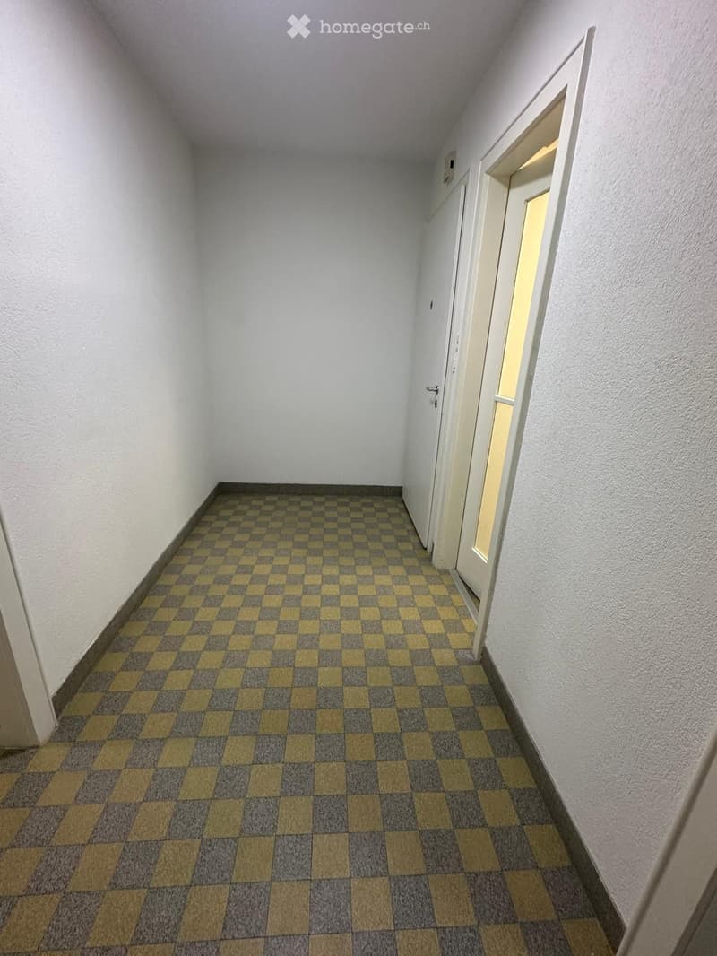 Empty hallway with checkered floor and white walls, featuring a door at the end.