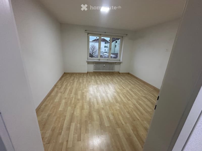 Empty room with wooden flooring, white walls, and a window with a radiator below it.