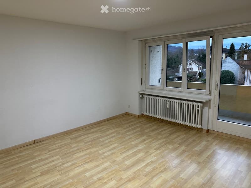 Empty room with wooden flooring, white walls, large windows, radiator, and a sliding glass door leading to a balcony.
