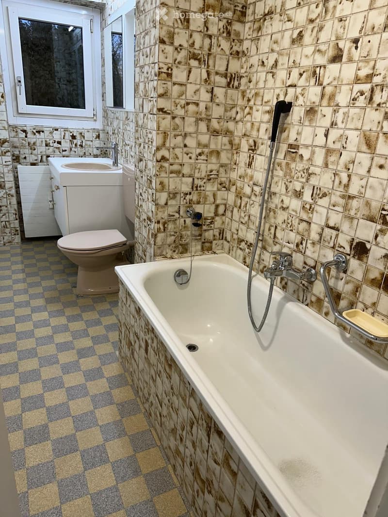 Bathroom with a bathtub, toilet, sink, and faucet. The walls are tiled with a marbled pattern, and the floor has a checkered tile design.