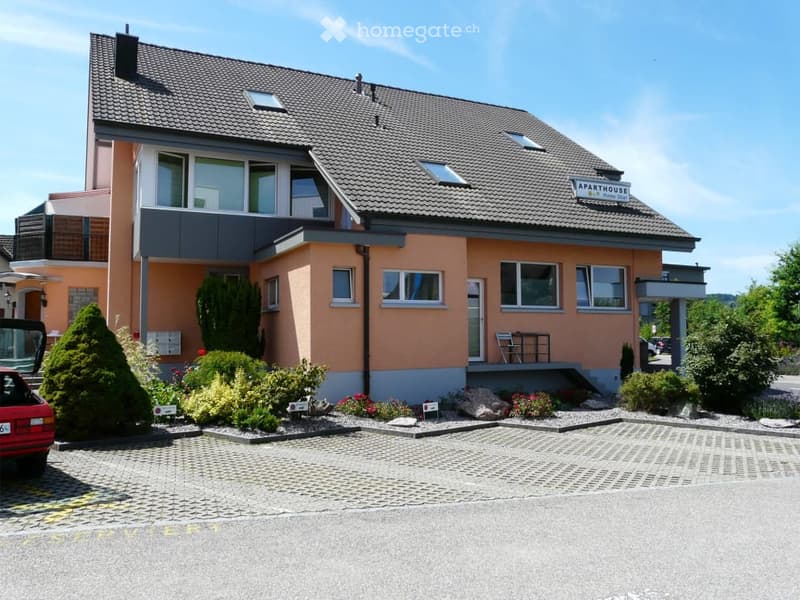 Two-story apartment building with orange and gray facade, multiple windows, and a small balcony area with outdoor furniture.