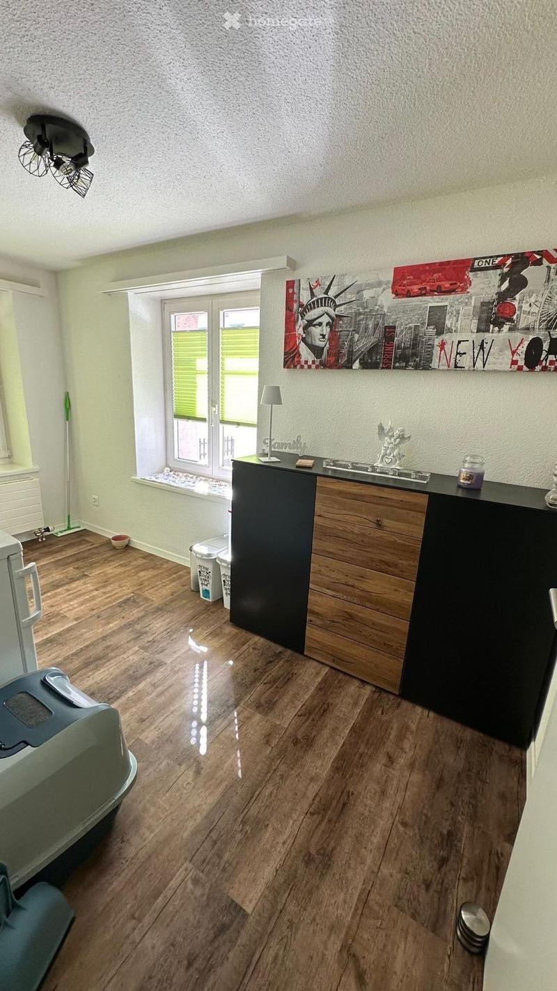 A modern, well-lit room with wooden flooring, a black table with a lamp, a refrigerator, and a fan on the ceiling.