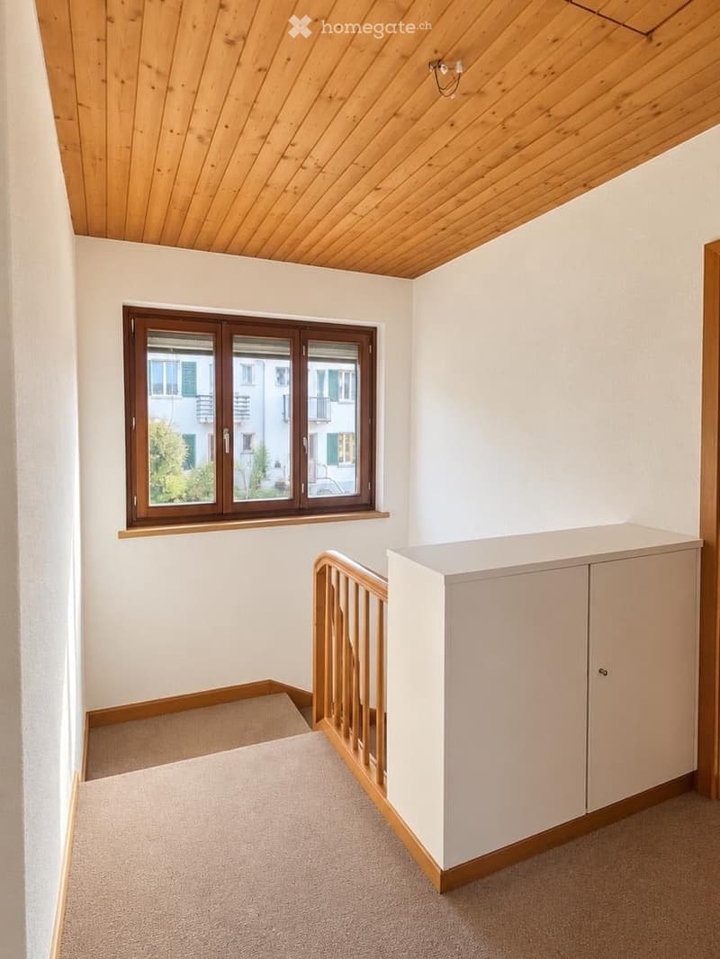 Empty room with wooden ceiling, large window, and small cabinet. No furniture or equipment present.