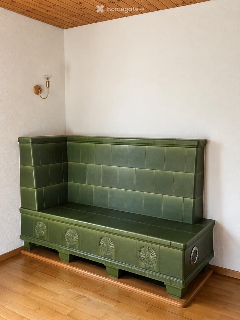 Green upholstered bench with decorative carvings, mounted on a wooden platform, against a white wall with a wall-mounted light fixture.