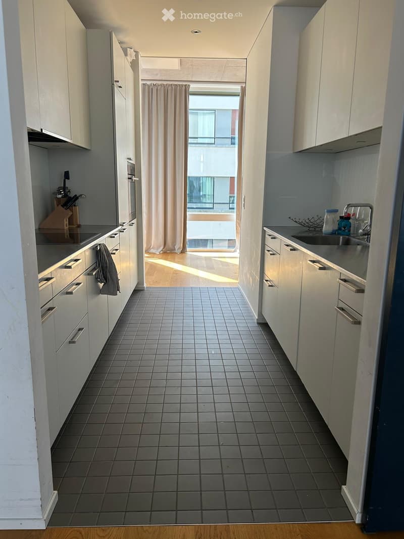 Modern kitchen with white cabinets, tiled floor, and a window with a curtain leading to a balcony.