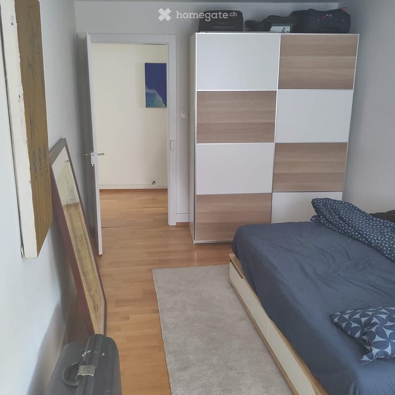 Cozy bedroom with a single bed, pillows, a modern wardrobe, a mirror, and a suitcase on the floor.