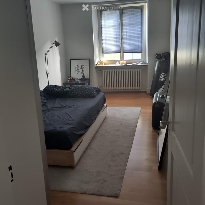 Minimalist bedroom with a platform bed, nightstand, table lamp, picture frame, radiator, suitcase, and punching bag in the corner.