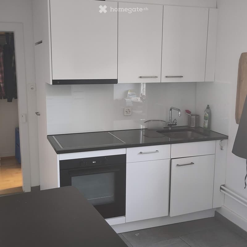 Modern kitchen with white cabinets, black countertop, built-in oven, and sink with faucet.