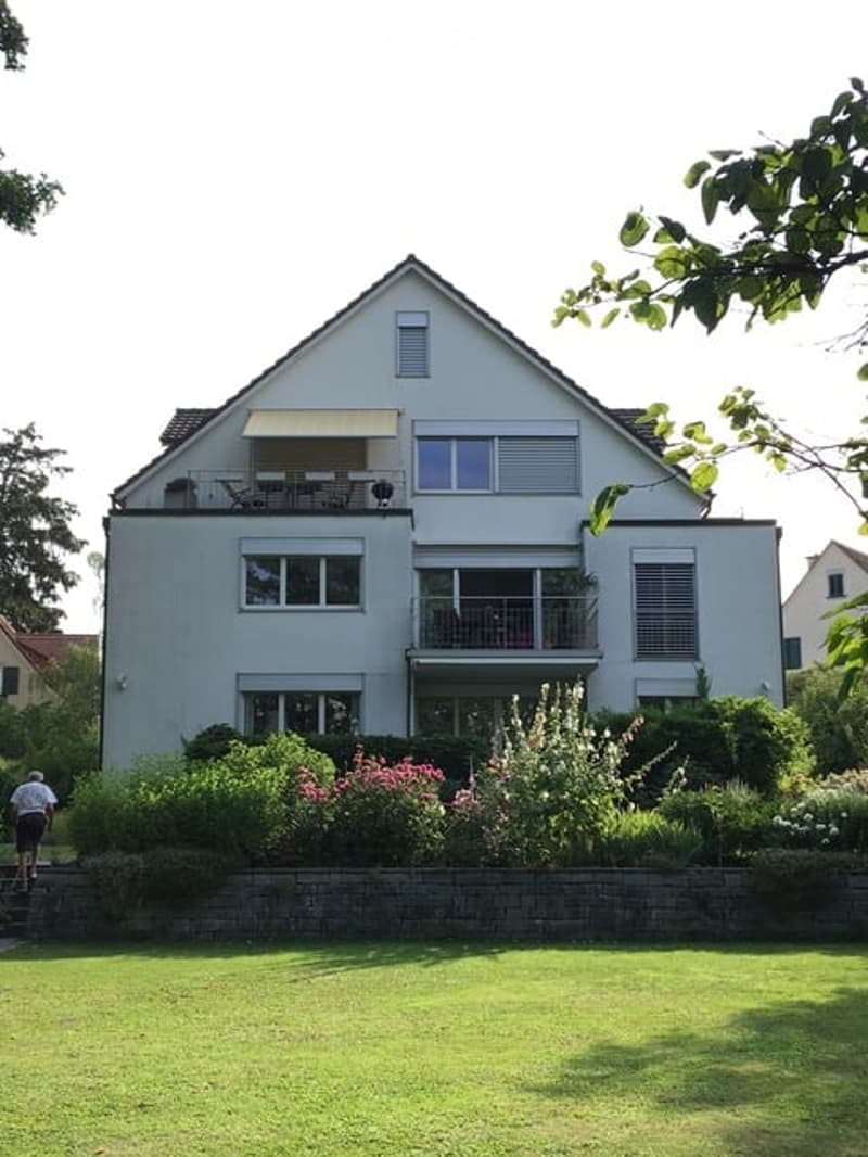 Two-story house with white exterior, multiple windows, balconies, and a well-maintained garden.