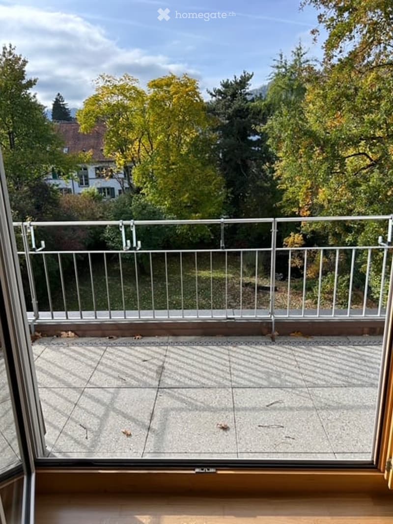 Balcony with metal railing, tiled floor, and view of trees and houses.