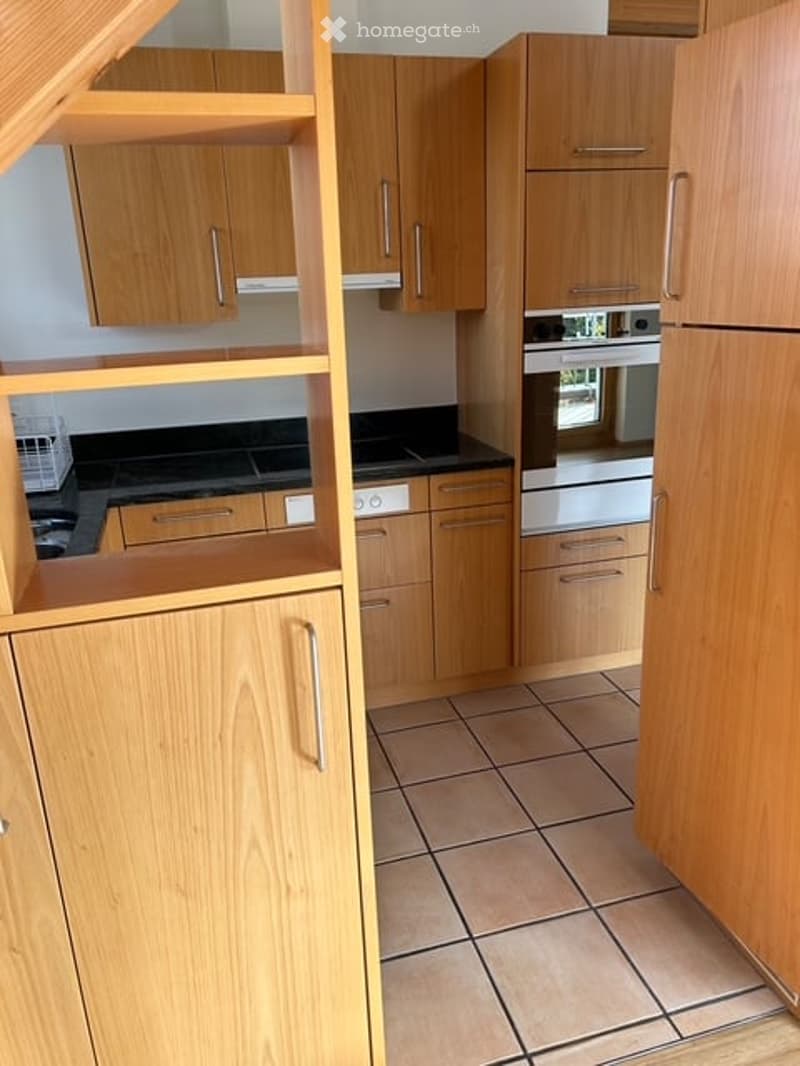 Modern kitchen with light wooden cabinets, stainless steel appliances, and tiled flooring.