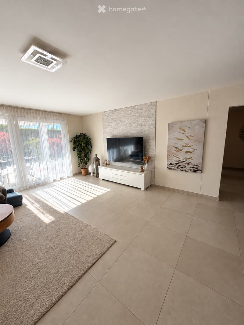 Bright living room with large windows, white brick accent wall, modern TV cabinet, sofa, coffee table, and artwork.