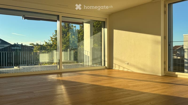 Empty room with wooden flooring and large glass sliding doors leading to an outdoor area. The space is well-lit with natural light and has a modern, minimalist design.