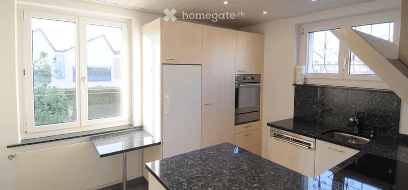 Modern kitchen with white cabinets, granite countertops, stainless steel appliances, and large windows offering a view of the exterior.