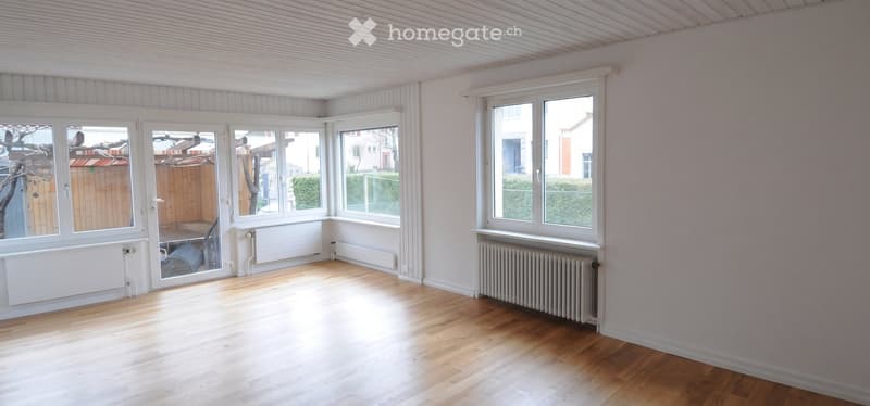 Bright, unfurnished room with wooden flooring, large windows, and radiators. The room has a modern, minimalist design with white walls and a slanted ceiling.