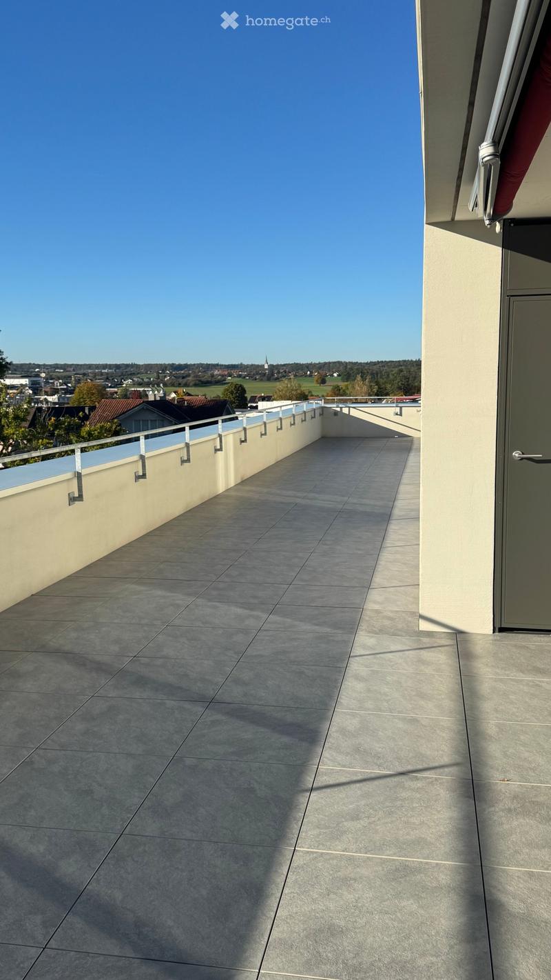 Modern balcony with grey tiled flooring, white railing, and a view of the surrounding landscape.