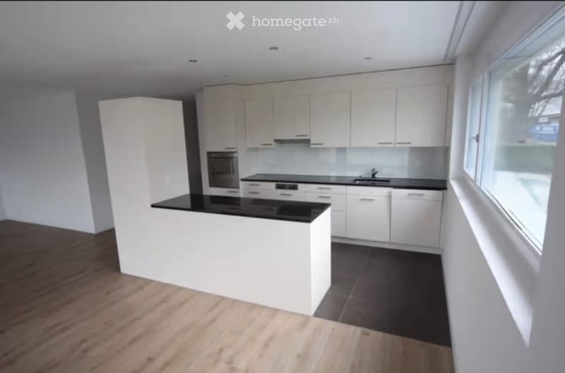 Modern kitchen with white cabinets, black countertops, and a central island. Features include a sink, oven, and ample natural light from large windows.