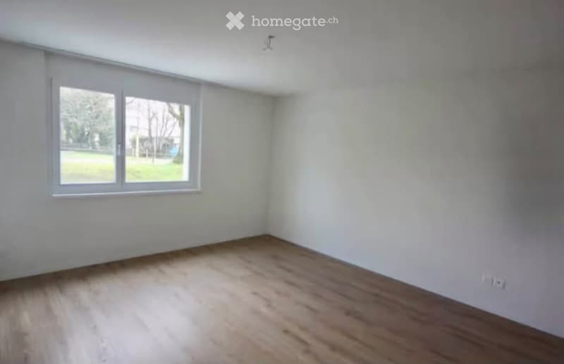 Empty room with white walls, wooden flooring, and a large window letting in natural light. No furniture or equipment present.