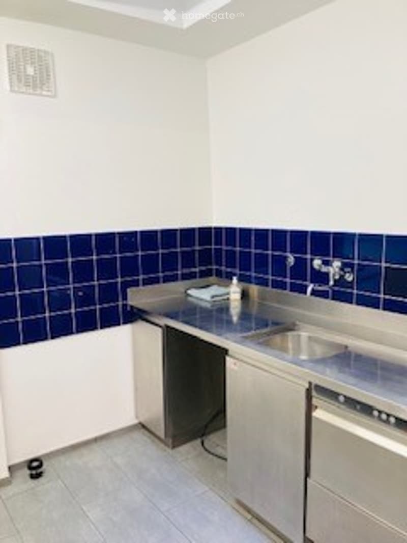 Stainless steel kitchen with a sink, faucet, and cabinets. The walls are tiled in blue and white, and the floor is tiled in light gray.