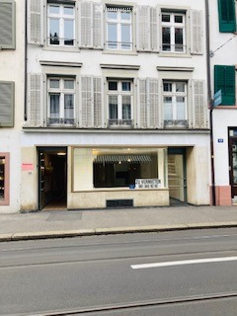 Multi-story building with classic European architecture, large windows with shutters, ground floor storefront with signage, and a small awning above the entrance.