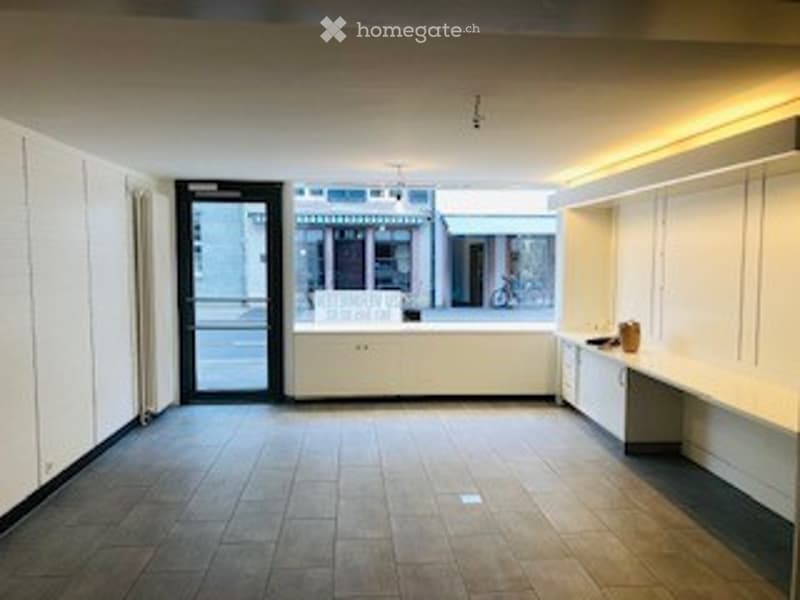 Empty room with white walls, wooden floor, large windows, and a door leading outside. No furniture or equipment present.
