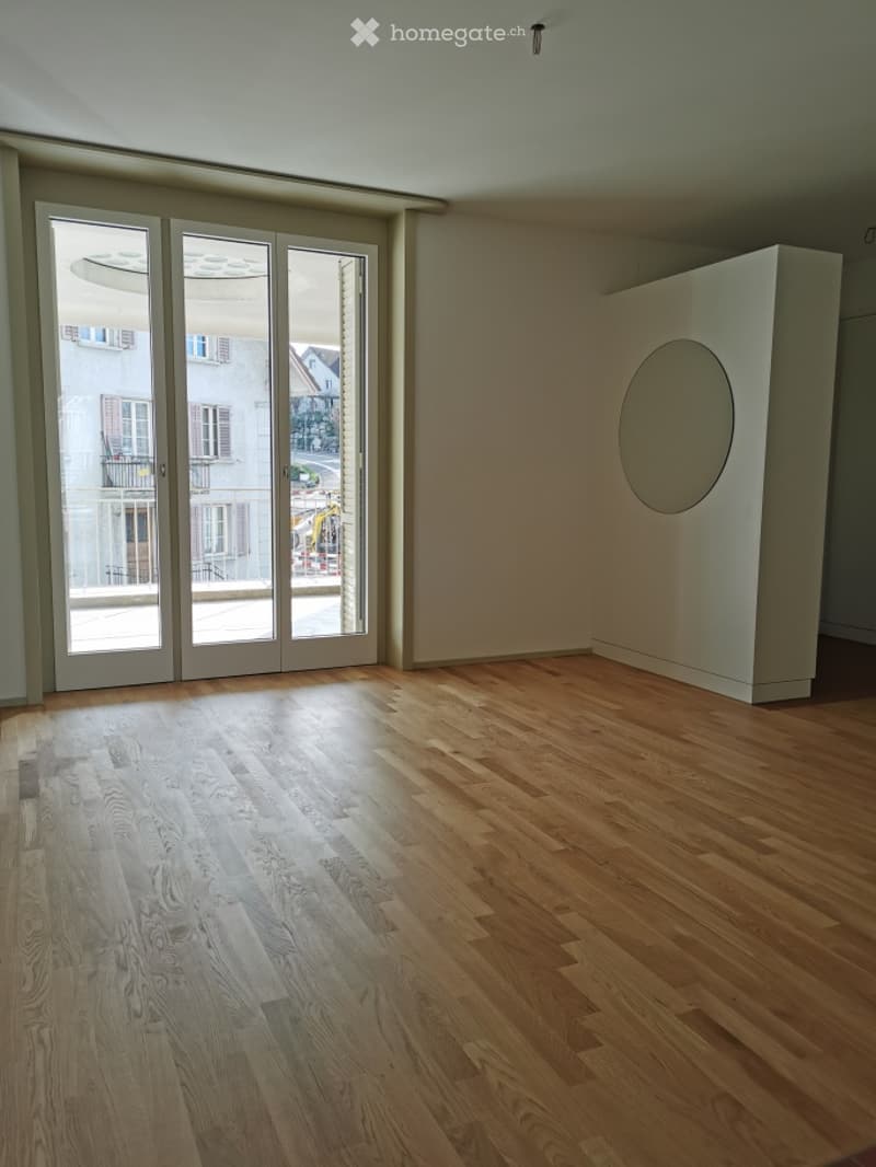 Empty room with wooden flooring, large glass sliding doors, and a white partition with a circular cutout.