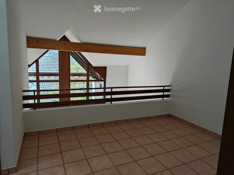 Balcony with wooden railing, tiled floor, and large windows offering a view of the roof and surrounding greenery.