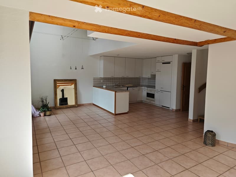 Open-plan kitchen and living area with tiled flooring, white cabinets, stainless steel appliances, and a large mirror on the wall.