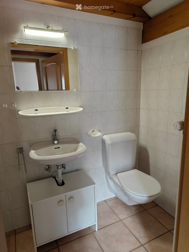 Modern bathroom with white tiles, a sink, toilet, mirror, and a small cabinet under the sink.