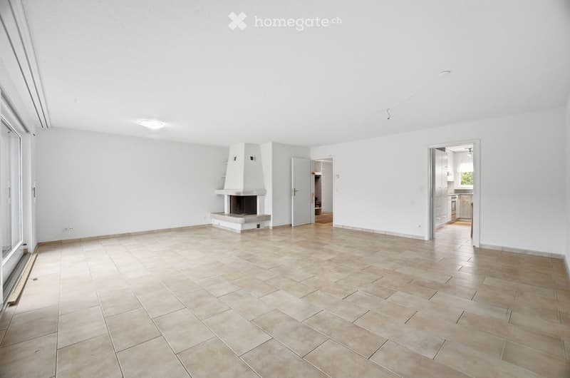 Empty living room with tiled floor, white walls, fireplace, large window, and open doorways to other rooms.