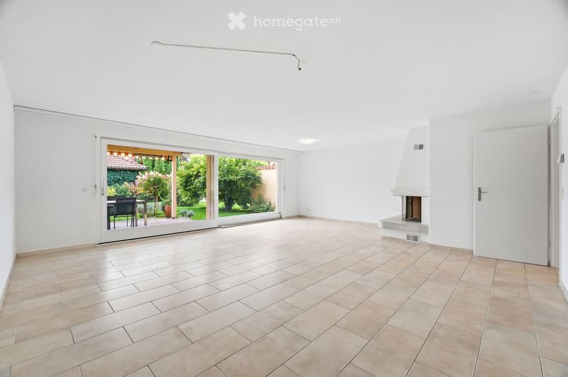 Empty room with tiled floor, white walls, fireplace, and large sliding glass door leading to a garden area.