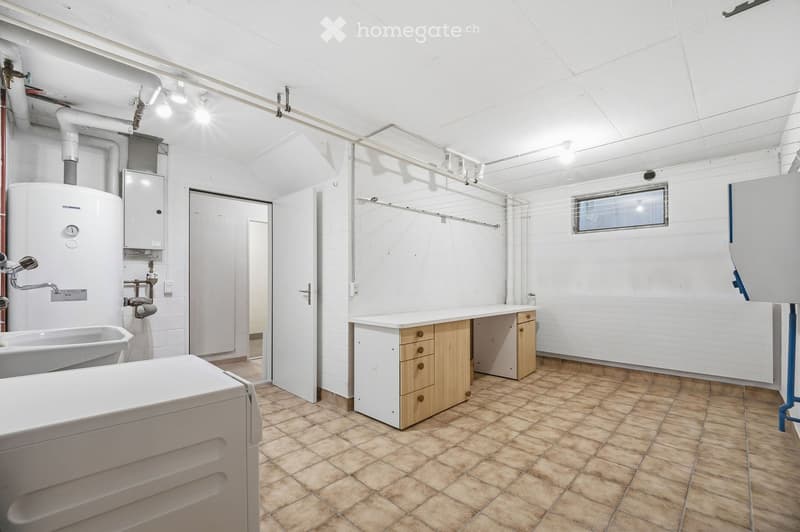 Bright bathroom with tiled floor, white walls, bathtub, washing machine, water heater, sink, and wooden cabinet.