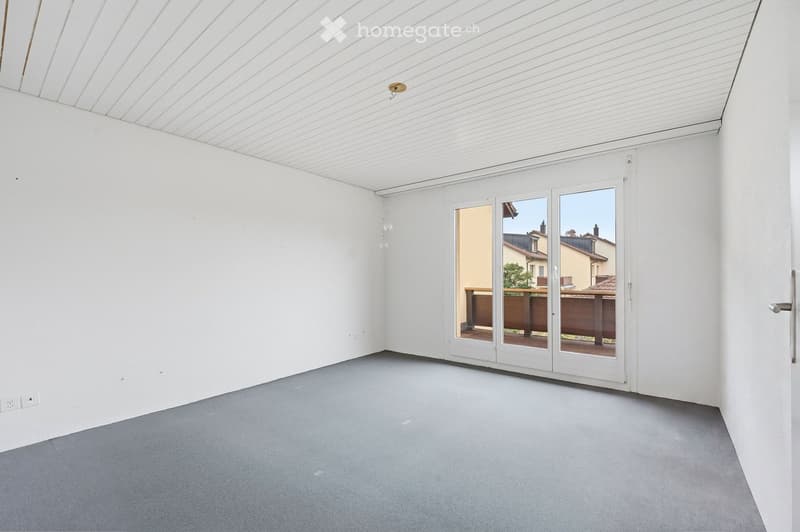 Empty room with white walls, grey carpeted floor, and large sliding glass doors leading to an outdoor area.