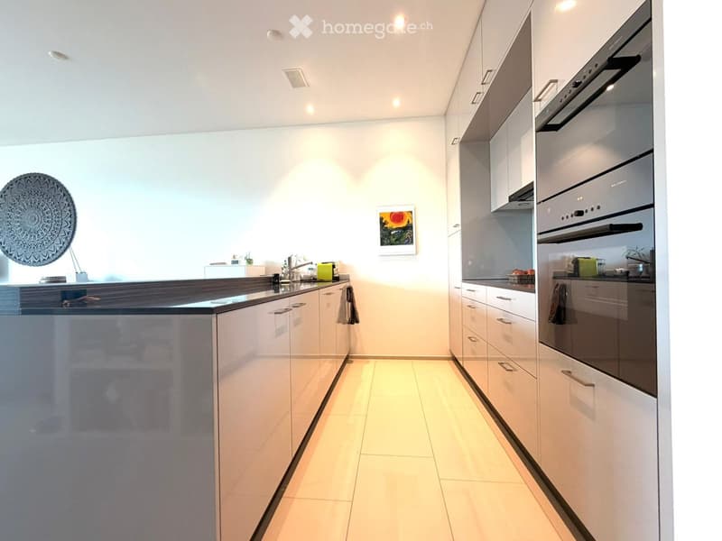 Modern kitchen with white cabinets, stainless steel oven, dark countertop, and decorative wall pieces.