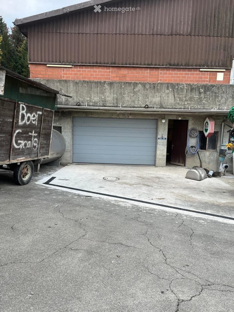 Two-story building with a large garage door, concrete walls, and a wooden trailer on the left side.