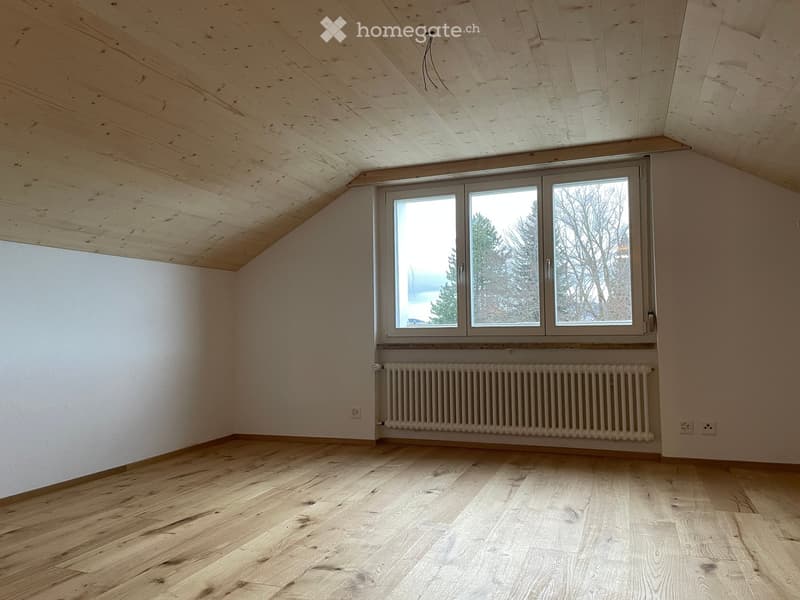 Empty room with wooden flooring, white walls, and a large window with a radiator below it.