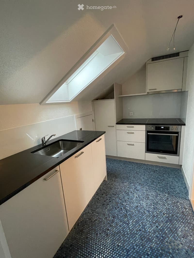 Modern kitchen with white cabinets, black countertops, a stainless steel sink, and an oven. The floor features a blue mosaic tile pattern.