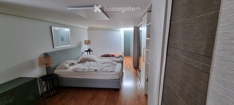 Cozy bedroom with a double bed, nightstand, lamp, and a small stool. The room features wooden flooring and a built-in wardrobe with mirrored doors.