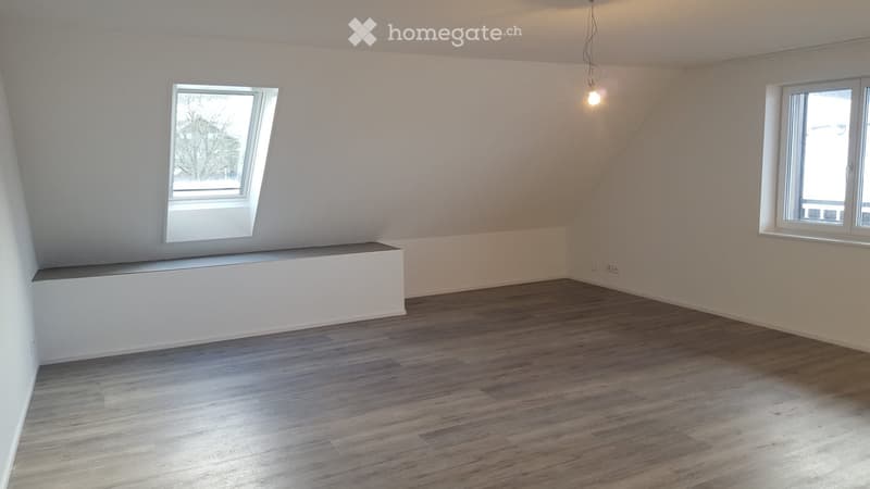 Empty room with wooden flooring, white walls, and two windows, one of which is a skylight. The room has a built-in bench along one wall.