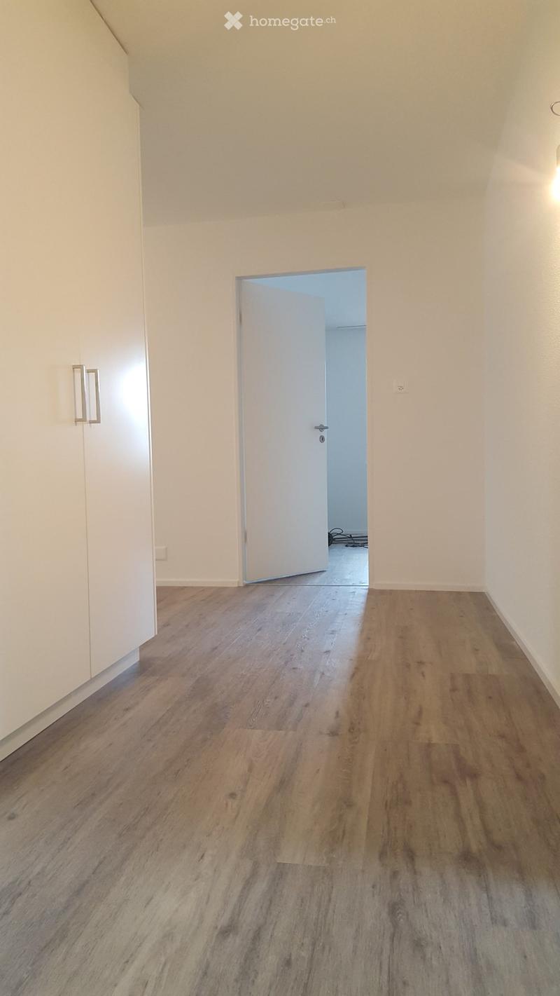 Empty room with wooden flooring and white walls, featuring a door leading to another room.