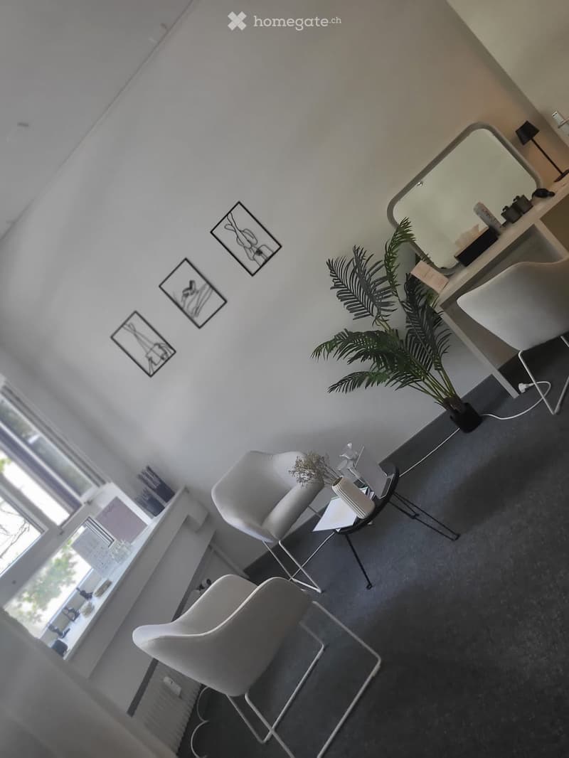 Modern, minimalist room with white chairs, a small round table, a large mirror, a potted plant, and a lamp. The room features large windows and a sleek, contemporary design.