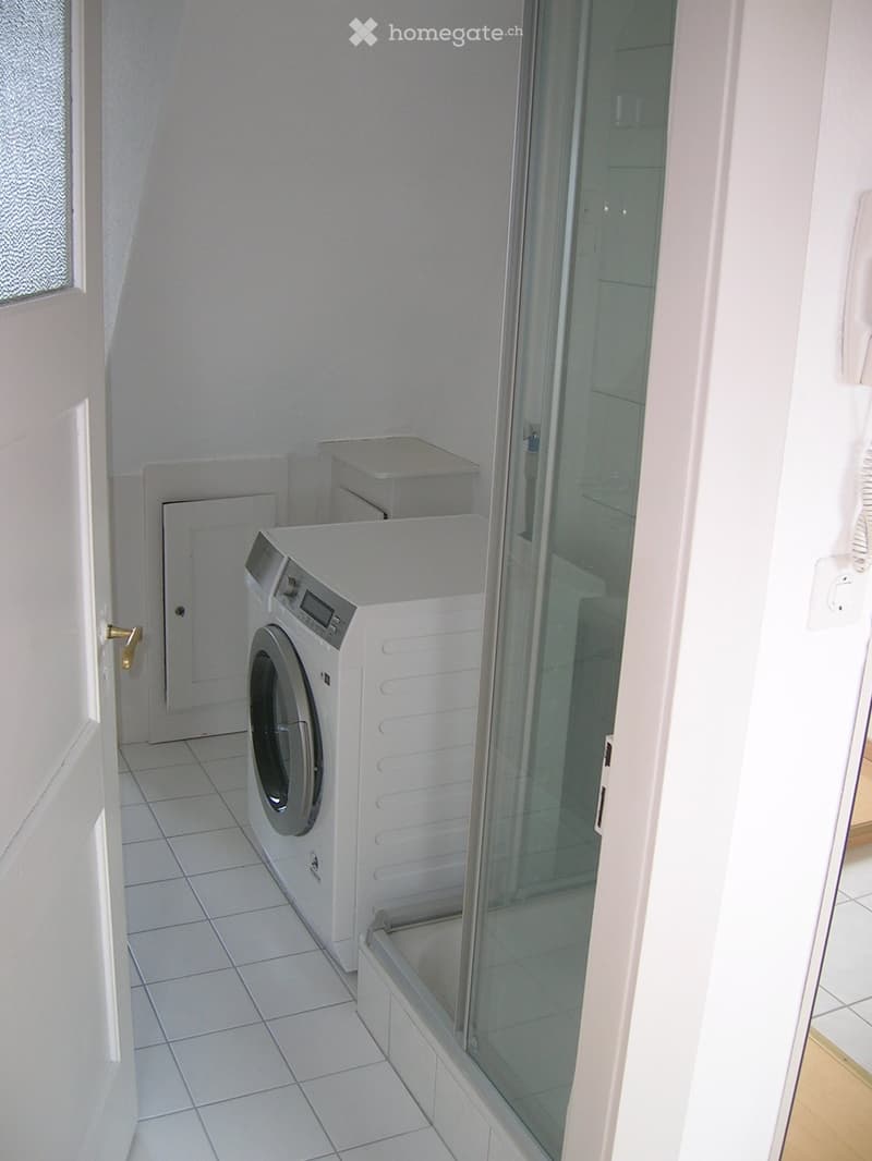 A small, tiled room with a white washing machine and a glass shower enclosure.
