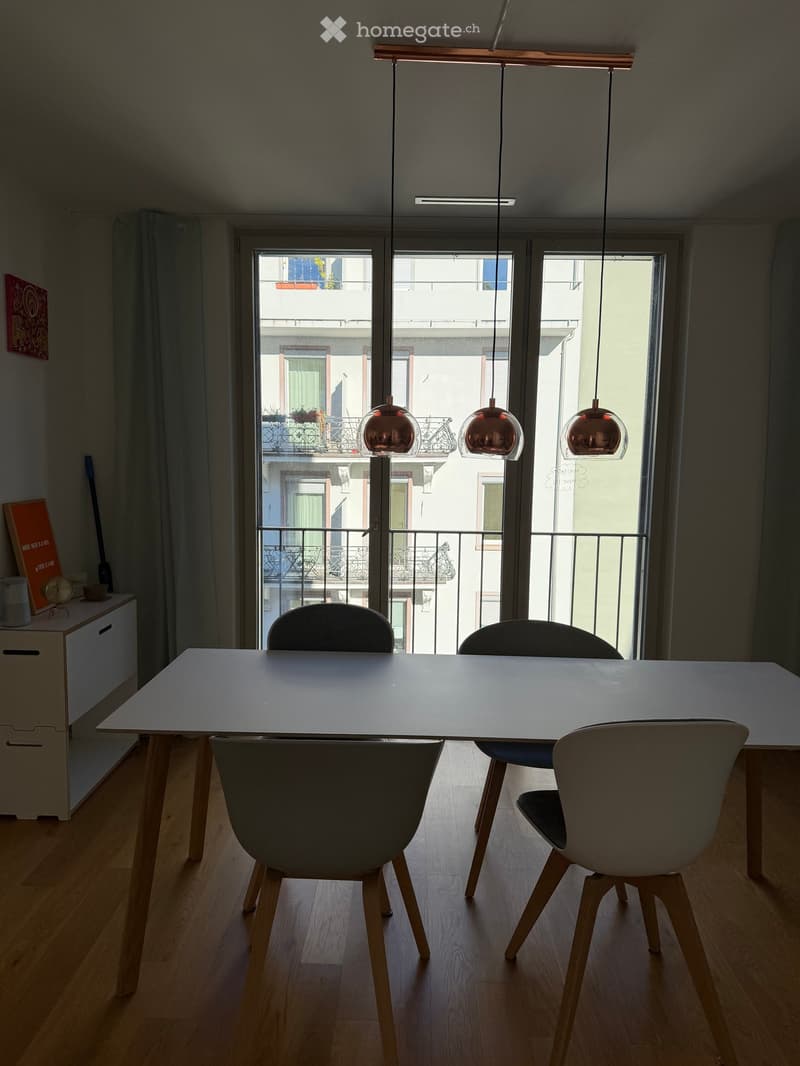 Dining area with a white table, four chairs, pendant lights, and a view of a balcony.