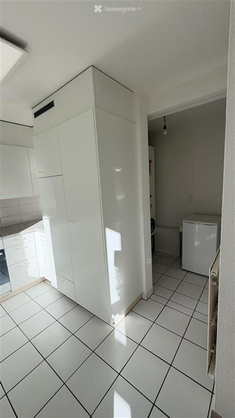 Bright, modern kitchen with white cabinets, tiled floor, and a private washing machine in the adjacent space.