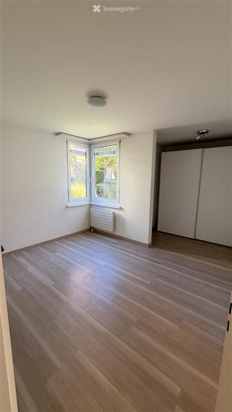 Empty room with wooden flooring, white walls, large window, radiator, and closet.
