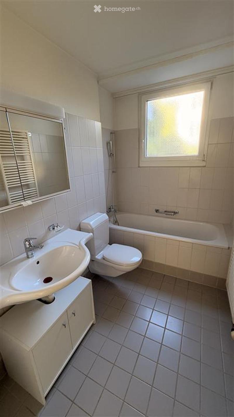 Modern bathroom with white tiles, a sink, toilet, bathtub, and a mirror above the sink.